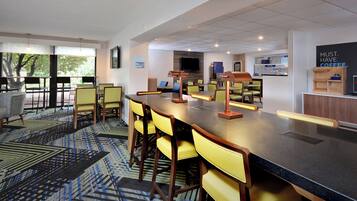 A modern bar area with a long counter, multiple chairs, and a television screen.