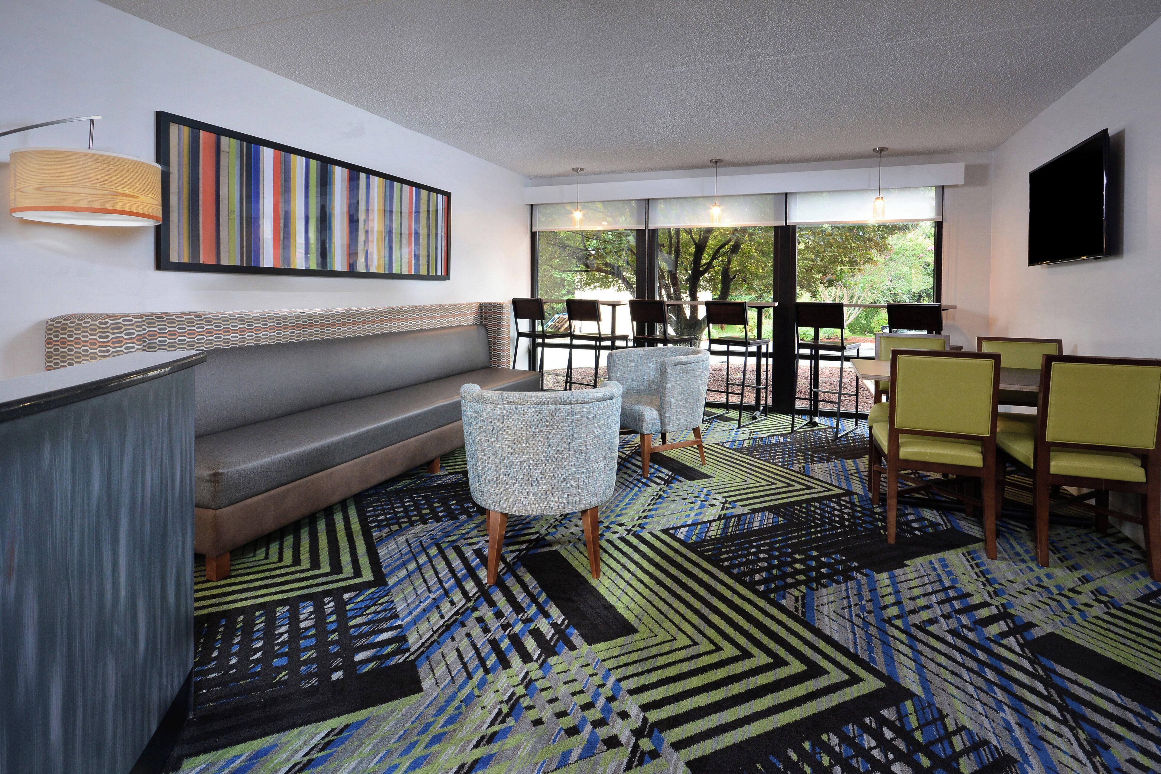 A modern lounge area with a sofa, chairs, a patterned rug, and a television.