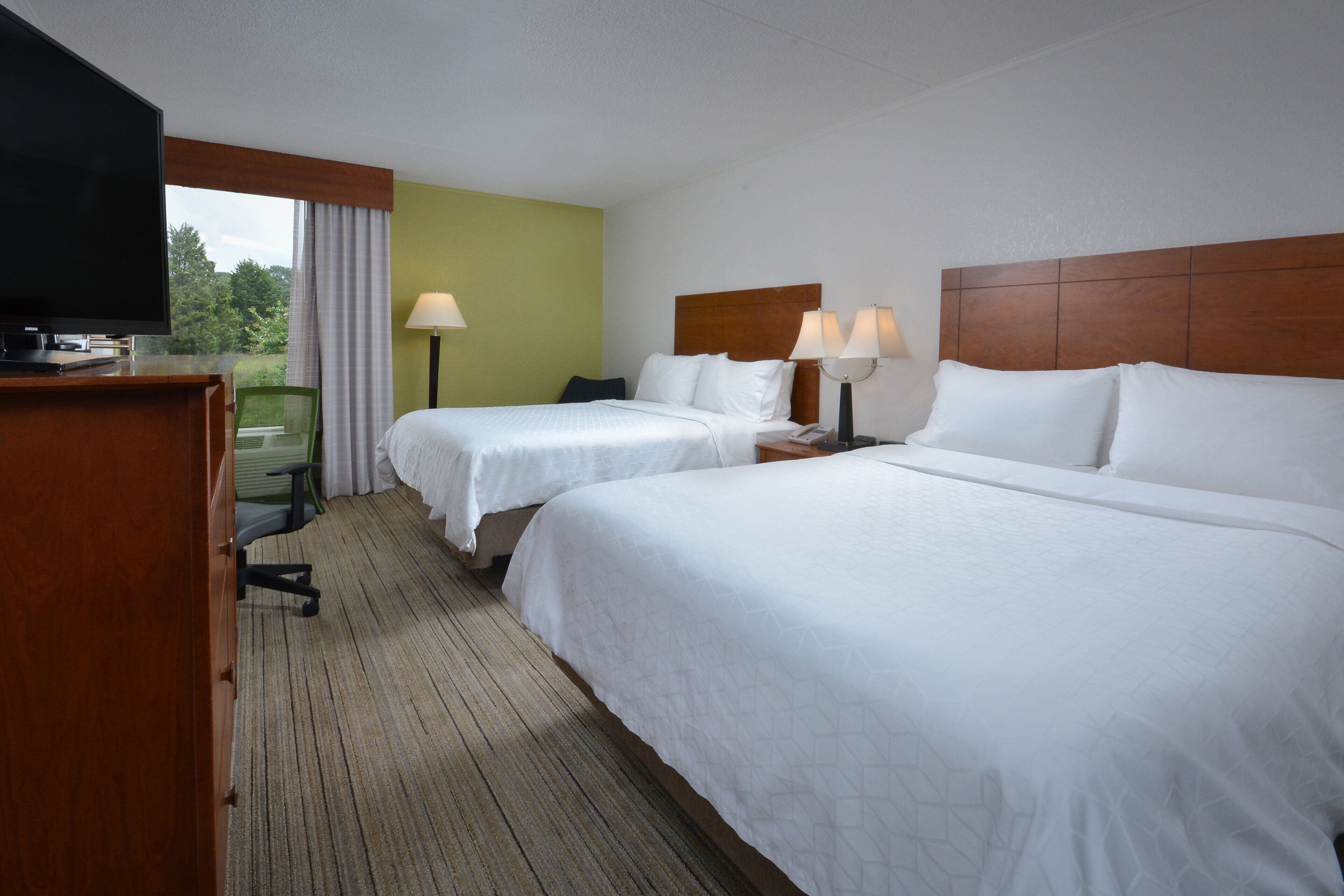 A hotel room with two beds, a TV, a desk, and a chair.