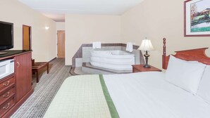 A hotel room with a bed, a TV, a desk, a lamp, a wooden headboard, a painting, and a bathroom with a bathtub and towels.