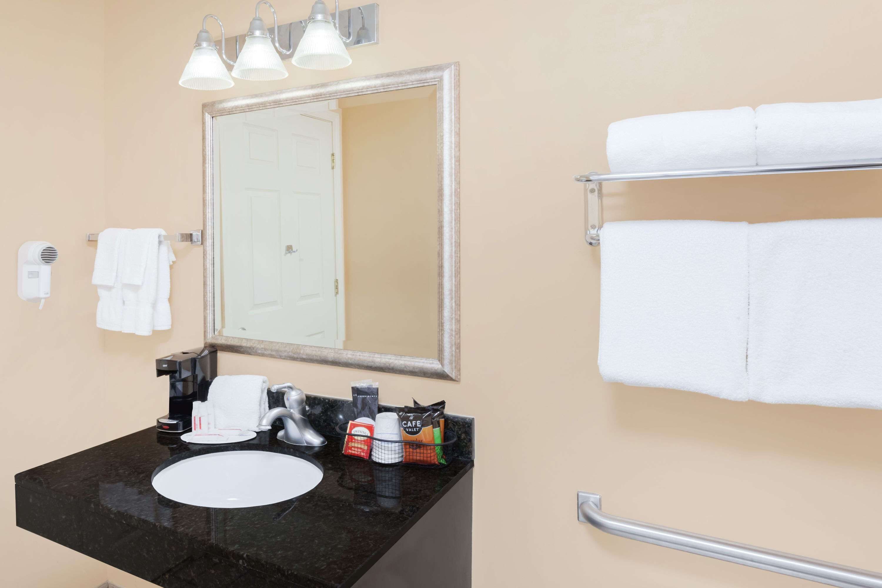 A bathroom with a black sink, a mirror, a towel rack with white towels, a coffee maker, and toiletries.