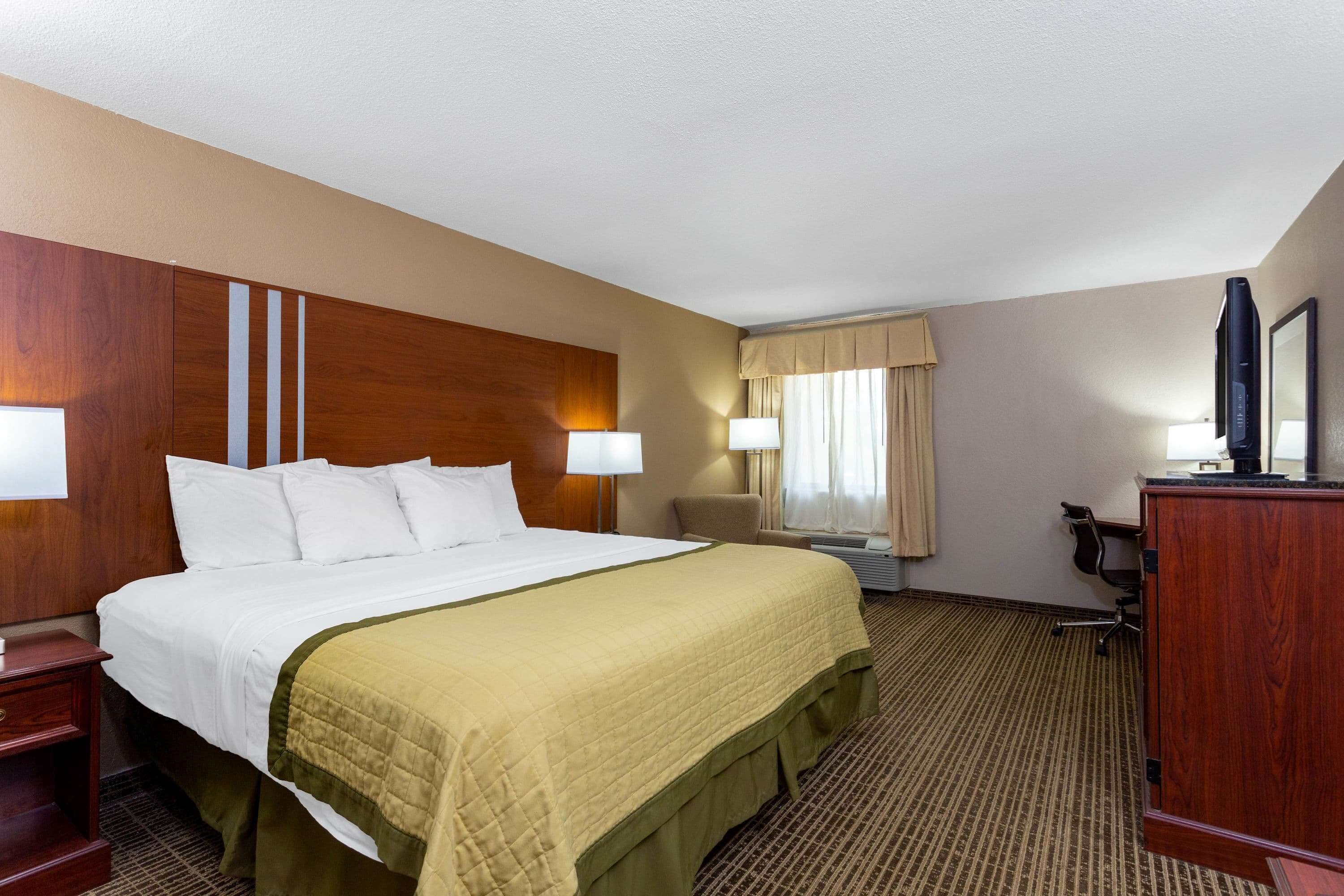 Une chambre d’hôtel avec un grand lit, deux tables de chevet, un bureau, une chaise, une armoire et une fenêtre avec des rideaux.