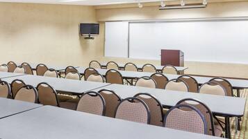 Una sala conferenze con più tavoli e sedie, una lavagna, uno schermo per proiettore e un televisore.