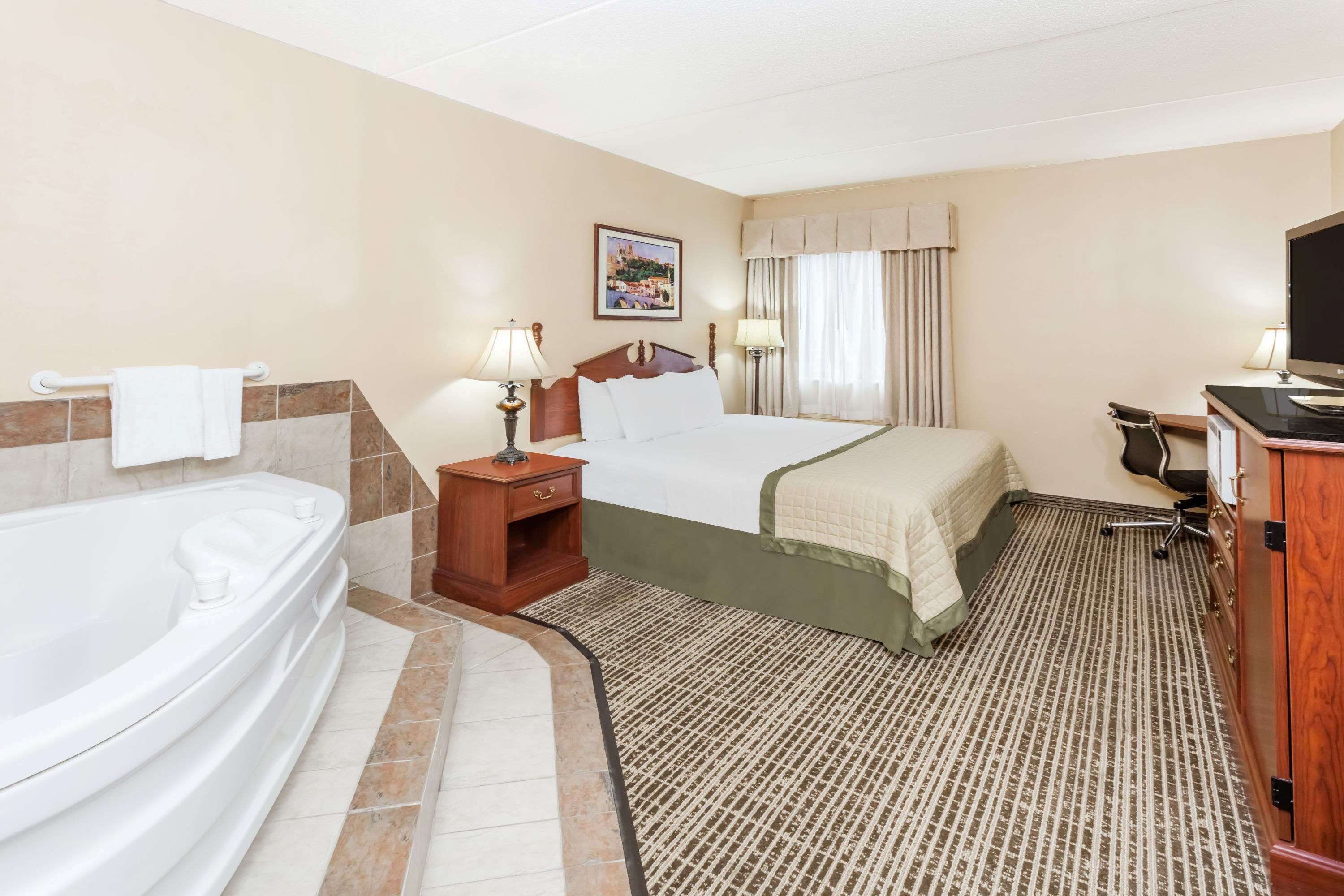 A hotel room with a large bathtub, a bed with a green bedspread, a desk with a computer, and a television.