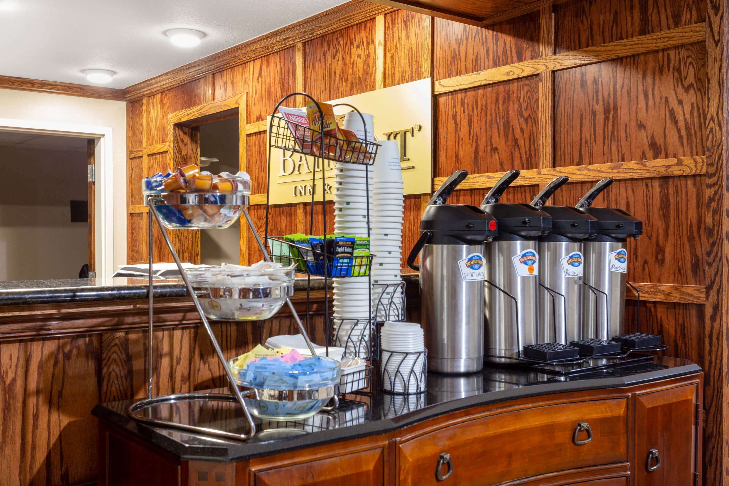 A buffet setup with a coffee station, a stack of plates, and a beverage dispenser.