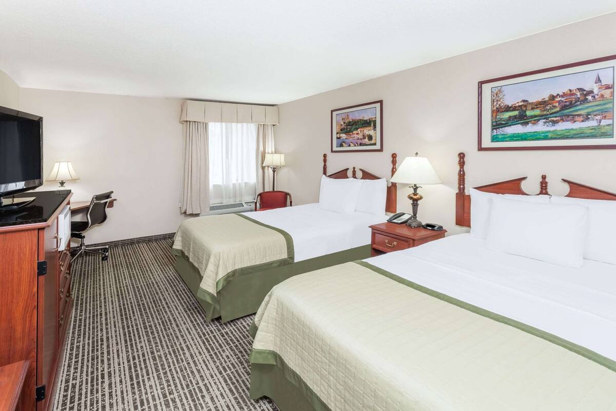 Une chambre d’hôtel avec deux lits, un bureau avec un ordinateur, une télévision et une fenêtre avec des rideaux.