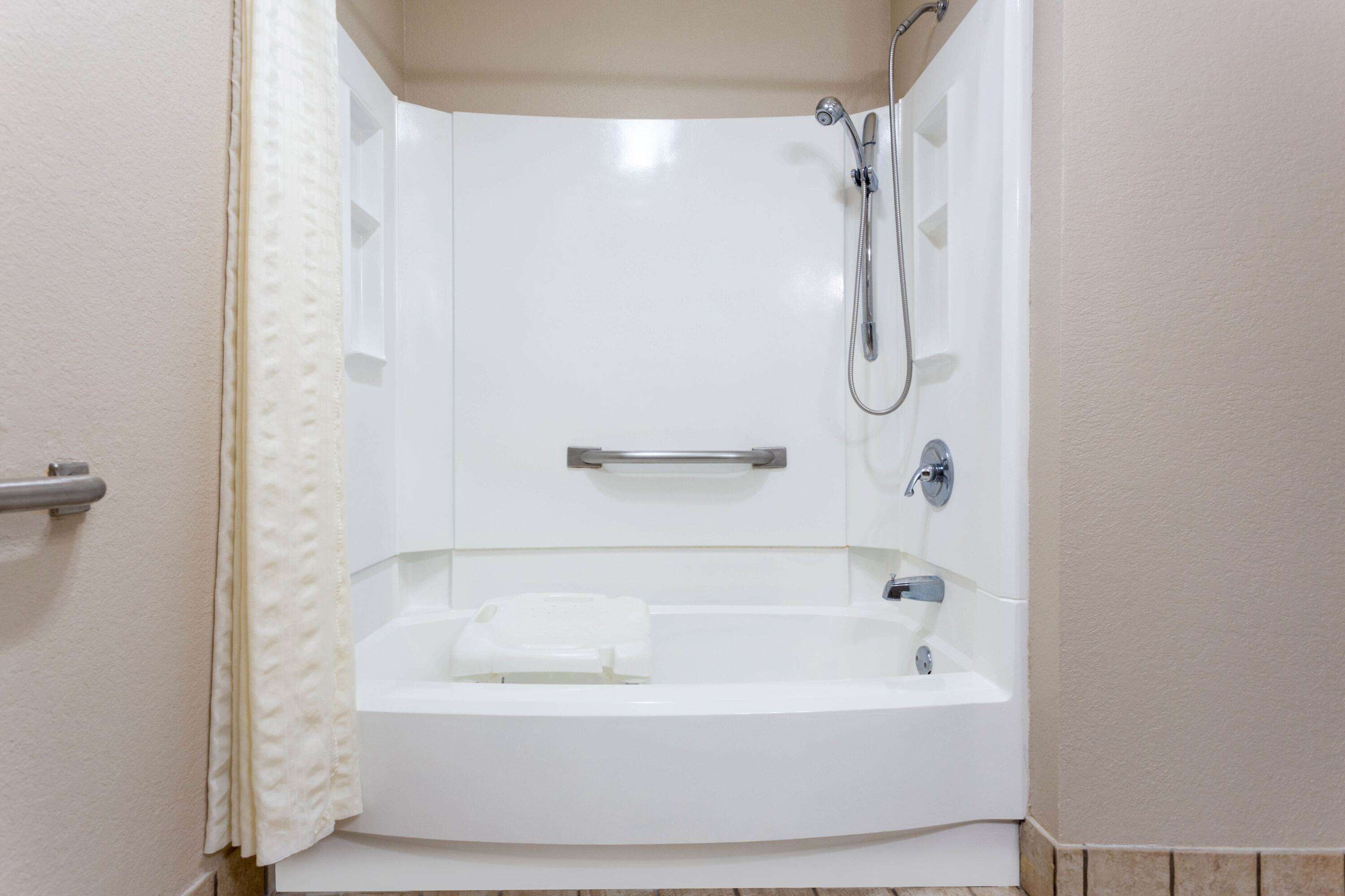 Une salle de bain d’angle équipée d’une baignoire, d’une douche et de barres d’appui.