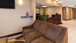 A hotel lobby with a brown sofa, a reception desk, a wall-mounted TV, and a large plant. - Best Western Springfield West Inn (West Springfield)