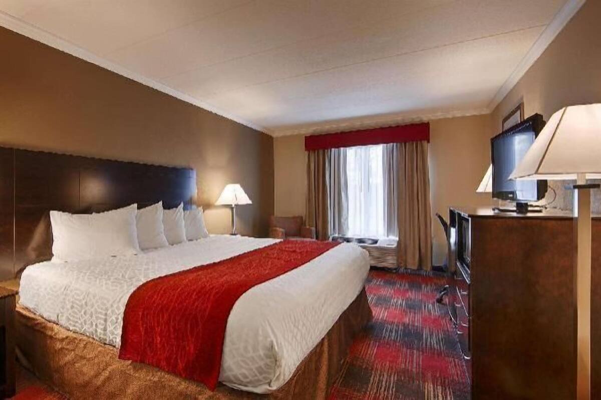 A hotel room with a large bed, two bedside lamps, a TV, and a window with curtains.