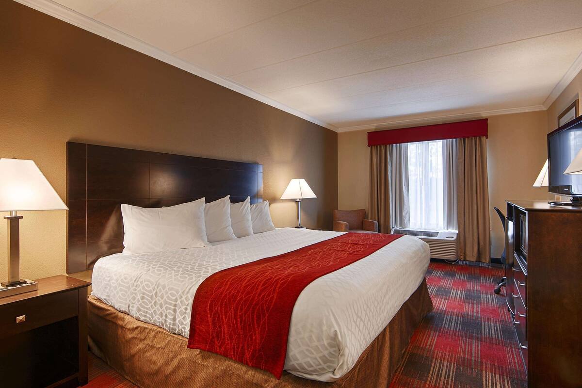 A hotel room with a large bed, two bedside lamps, a television, and a desk with a lamp.