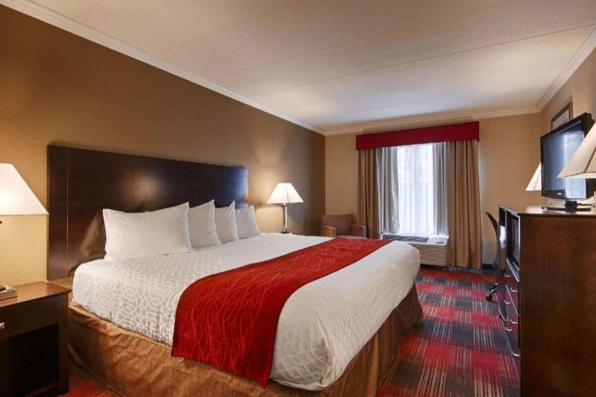 A hotel room with a large bed, two bedside lamps, a television, and a window with curtains.