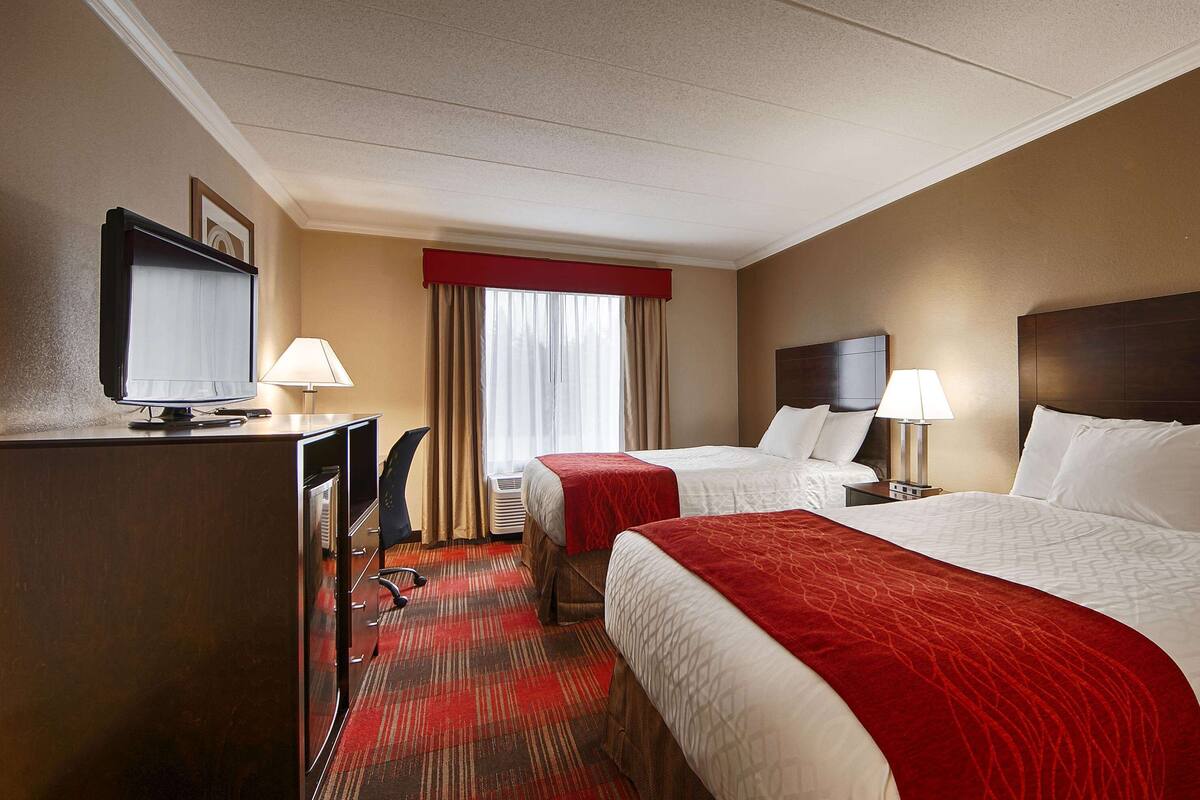 A hotel room with two beds, a desk with a computer, a TV, and a window with curtains.