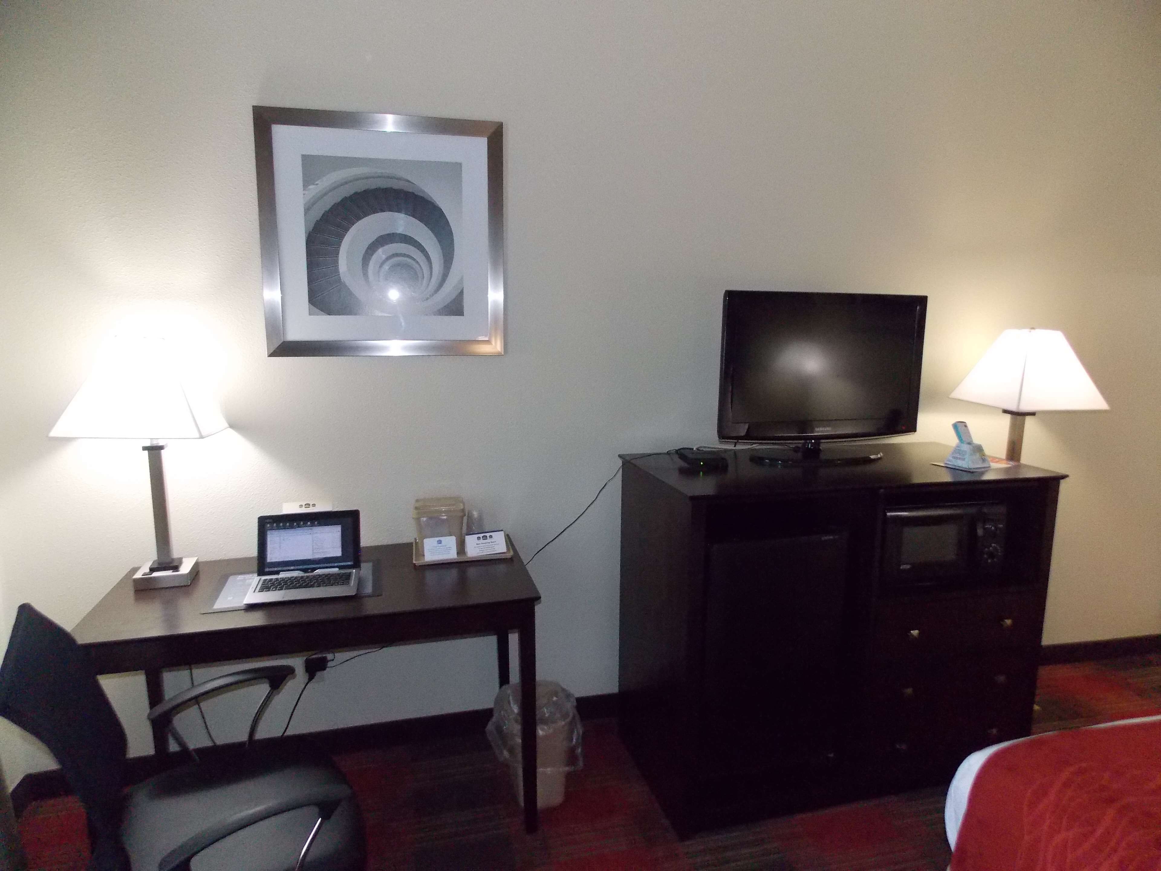 A hotel room with a desk, a television, a microwave, a chair, and a bed.