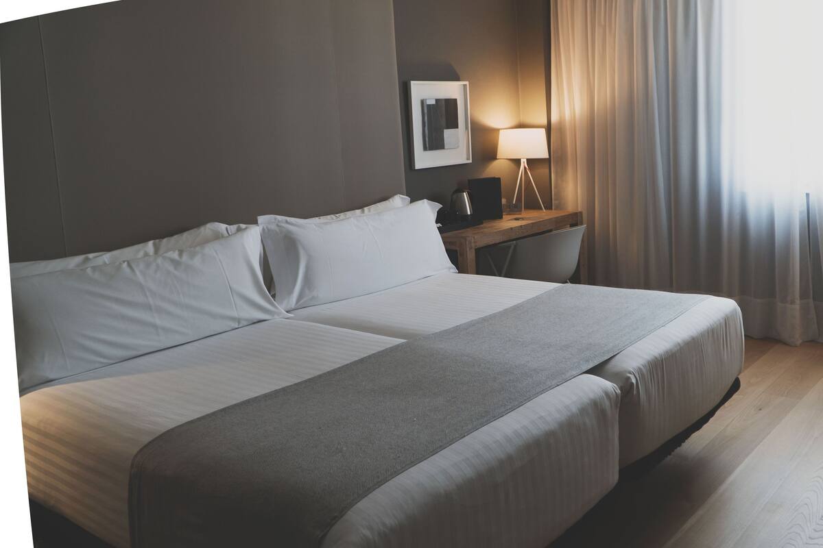 A hotel room with a large bed, a desk, a chair, and a lamp.