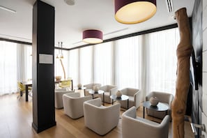 Un moderno vestíbulo de hotel con un área de estar central, un muro decorativo de madera y ventanas amplias.