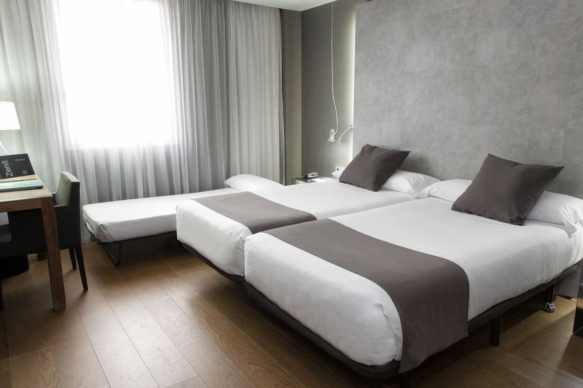 A hotel room with two beds, a desk, and a chair.