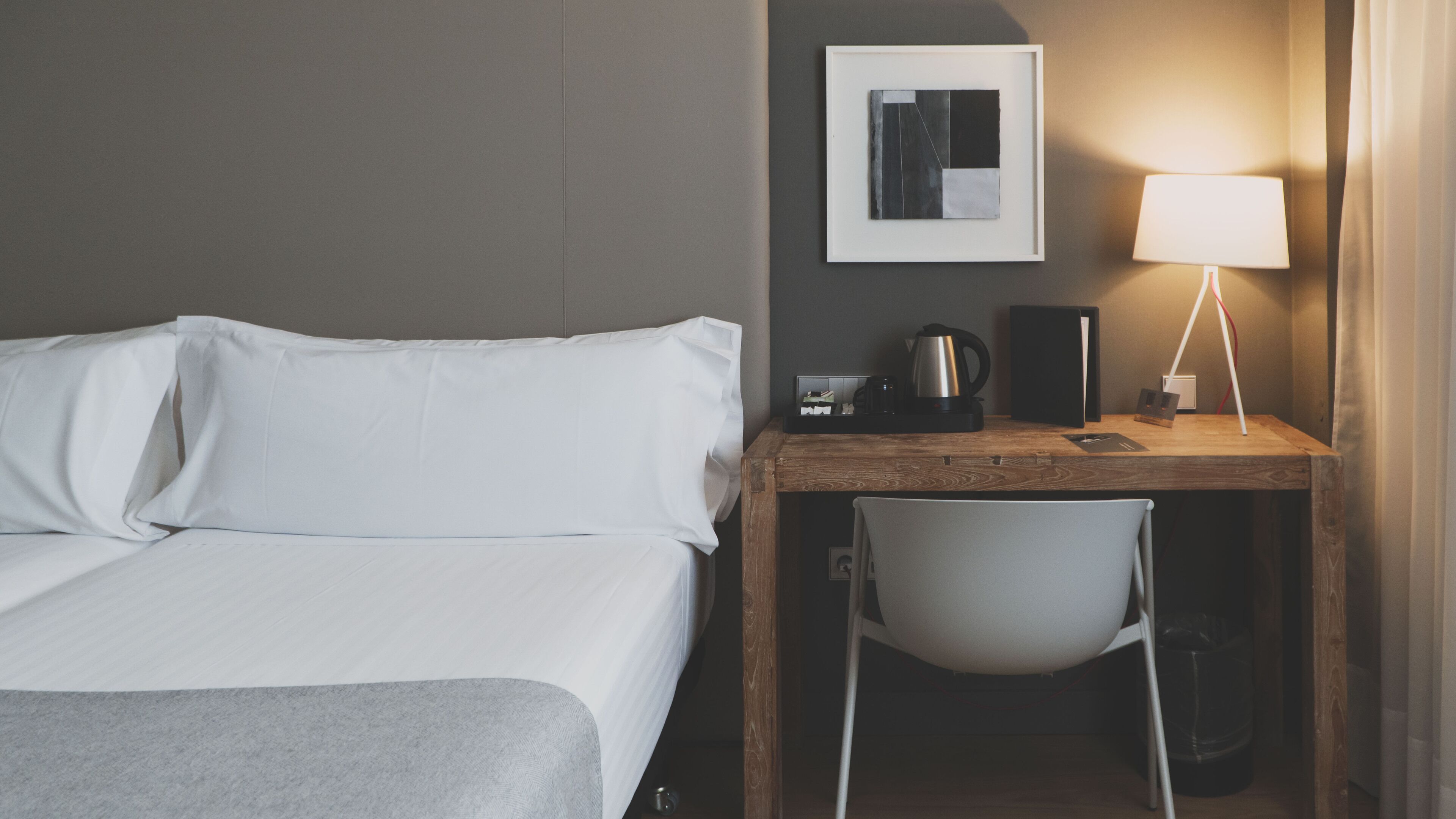 Ein Hotelzimmer mit einem Bett, einem Schreibtisch mit Stuhl, einer Lampe und einem gerahmten Bild an der Wand.
