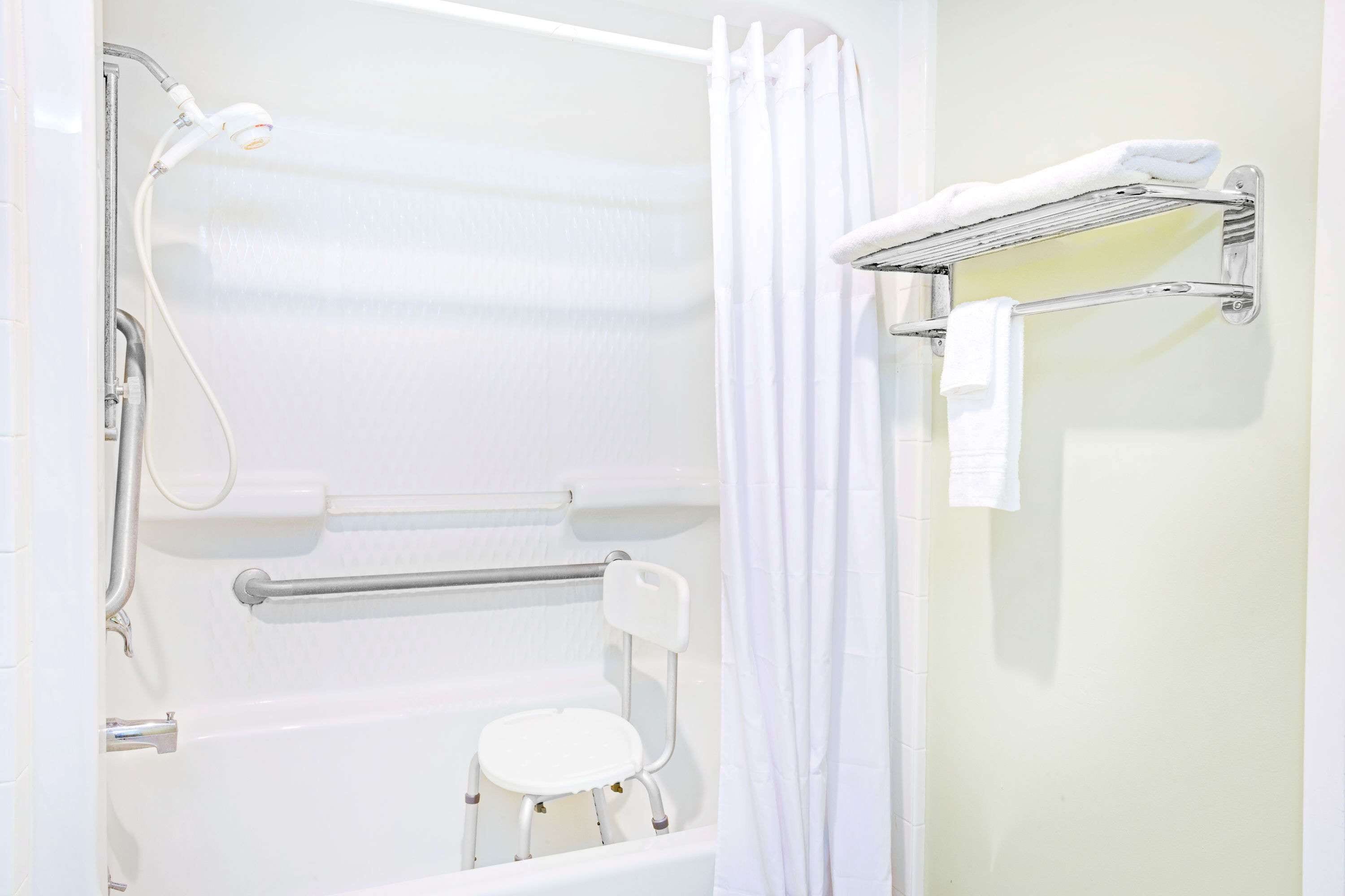 A bathroom with a white bathtub, a shower, a grab bar, a white towel rack, and a white towel on the rack.