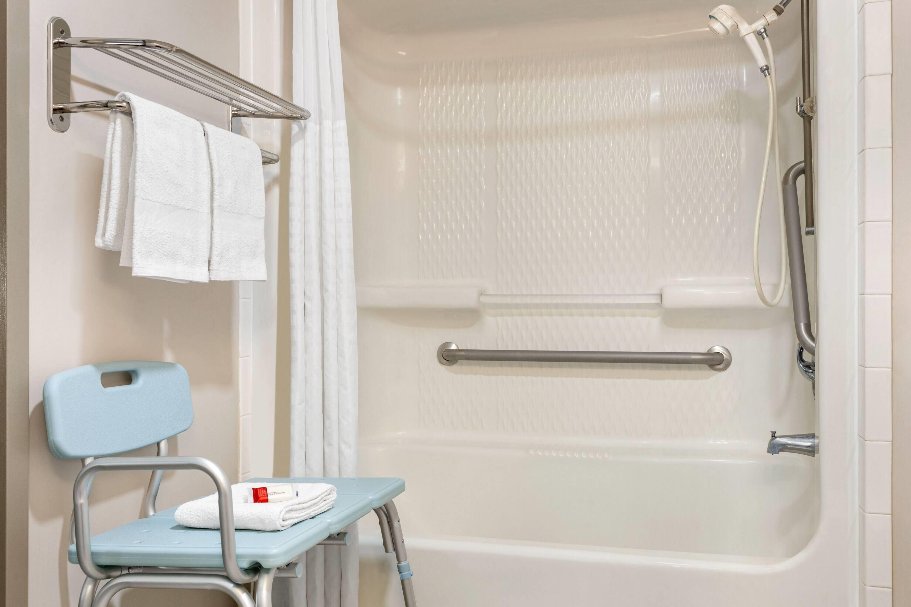 Ein Badezimmer mit Dusche, einer Haltestange, einem Handtuchhalter und einer rollstuhlgerechten Sitzbank.