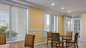 A dining area with a wooden table and chairs, large windows with blinds, and a yellow wall. - Days Inn by Wyndham Kingsland Naval Base I-95 (Kingsland)