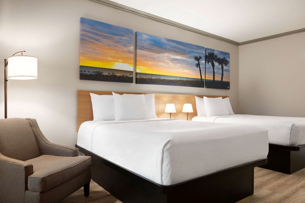 A hotel room with two beds, a chair, and two wall-mounted lamps.