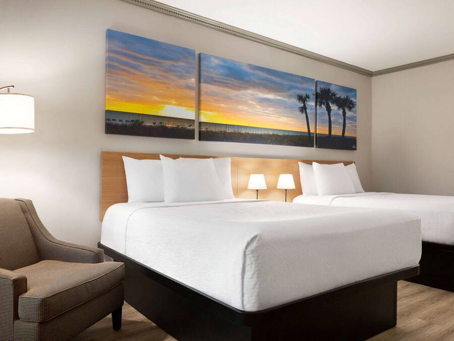 A hotel room with two beds, a chair, and two wall-mounted lamps.
