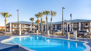 A swimming pool surrounded by a fence, with palm trees and a multi-story building in the background. - Days Inn by Wyndham Kingsland Naval Base I-95 (Kingsland)