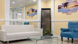 A reception area with a white sofa, a blue armchair, and a glass coffee table. There are two wall art pieces depicting tropical scenes. - Days Inn by Wyndham Kingsland Naval Base I-95 (Kingsland)