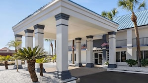 A hotel entrance with a covered walkway, palm trees, and American flags. - Days Inn by Wyndham Kingsland Naval Base I-95 (Kingsland)