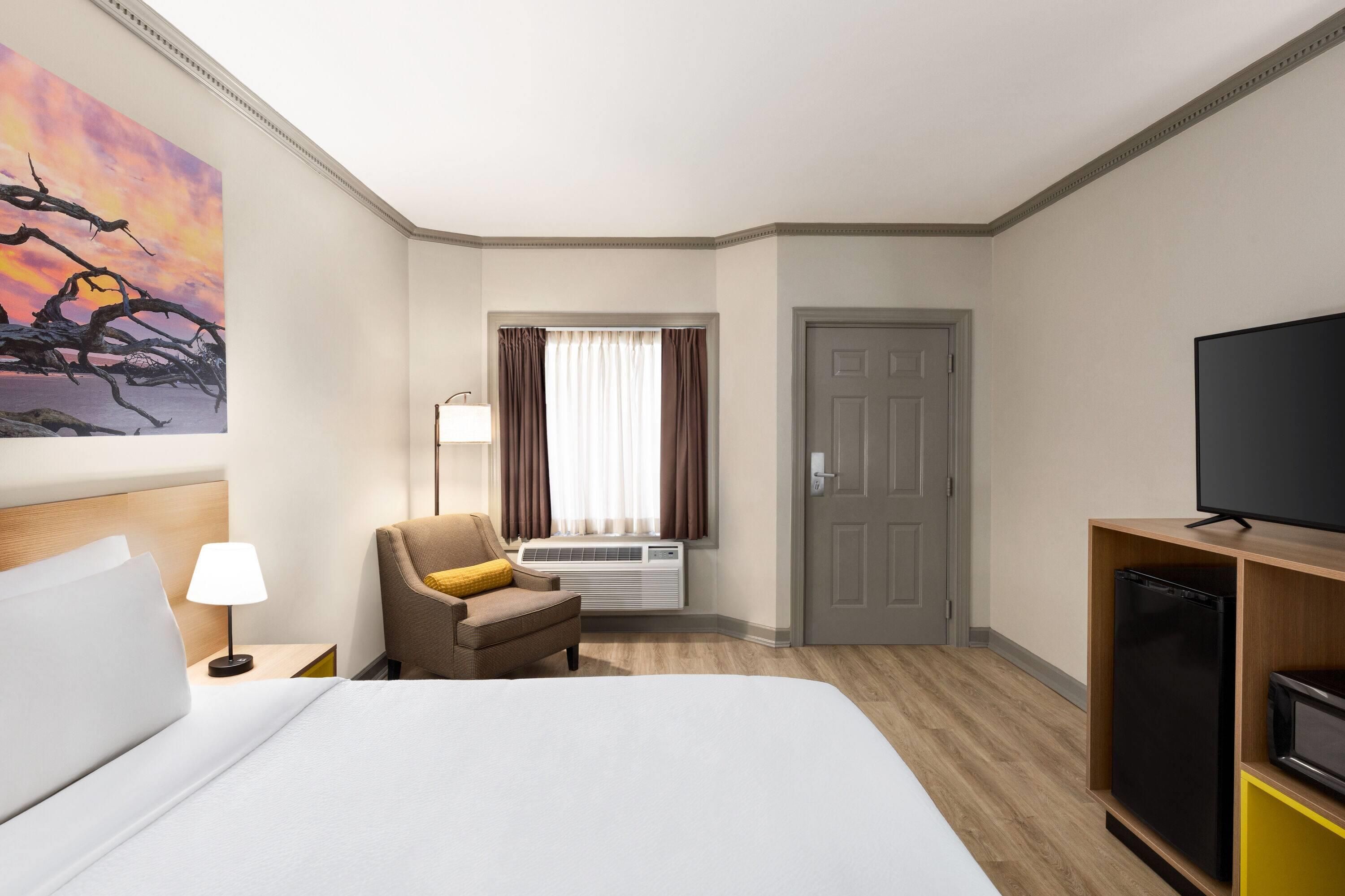 Ein Hotelzimmer mit einem Bett, einem Sessel, einem Fernseher, einer Klimaanlage und einer Tür.