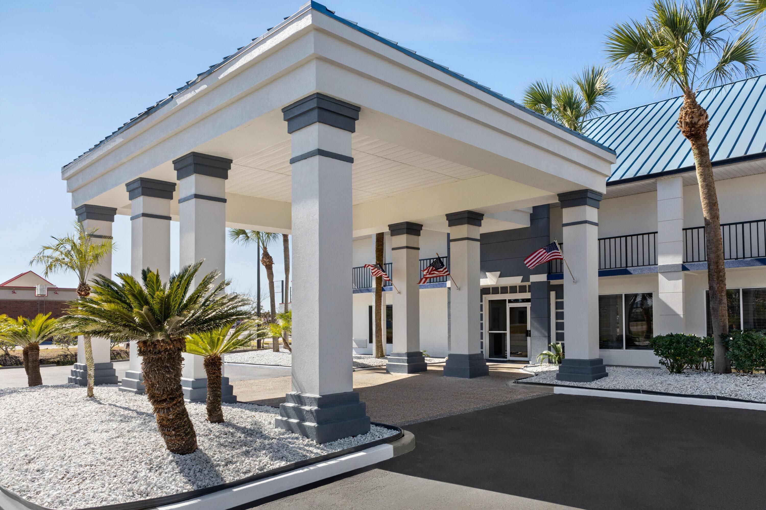 A hotel entrance with a covered walkway, palm trees, and American flags.