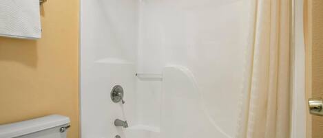 A small, enclosed shower area with a white bathtub, a toilet, and a towel rack.