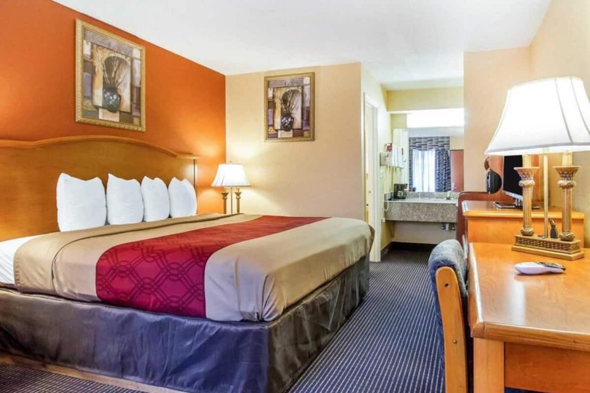 Een hotelkamer met een bed, nachtlampjes, een bureau en een spiegel.