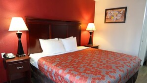 Une chambre d’hôtel avec un grand lit, deux lampes de chevet, une table de chevet avec un téléphone et une carte encadrée accrochée au mur.
