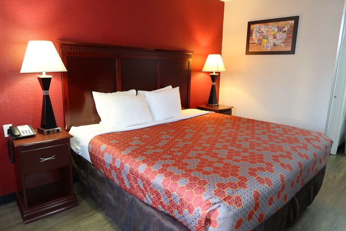 Een hotelkamer met een groot bed, twee bedlampen, een nachtkastje met een telefoon en een inlijsting kaart aan de muur.