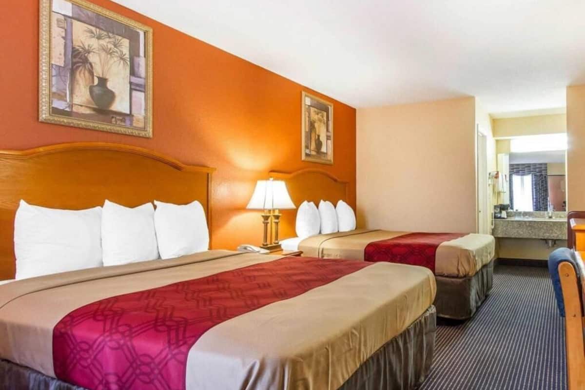 Een hotelkamer met twee bedden, een bureau, een stoel, een lamp en een schilderij aan de muur.
