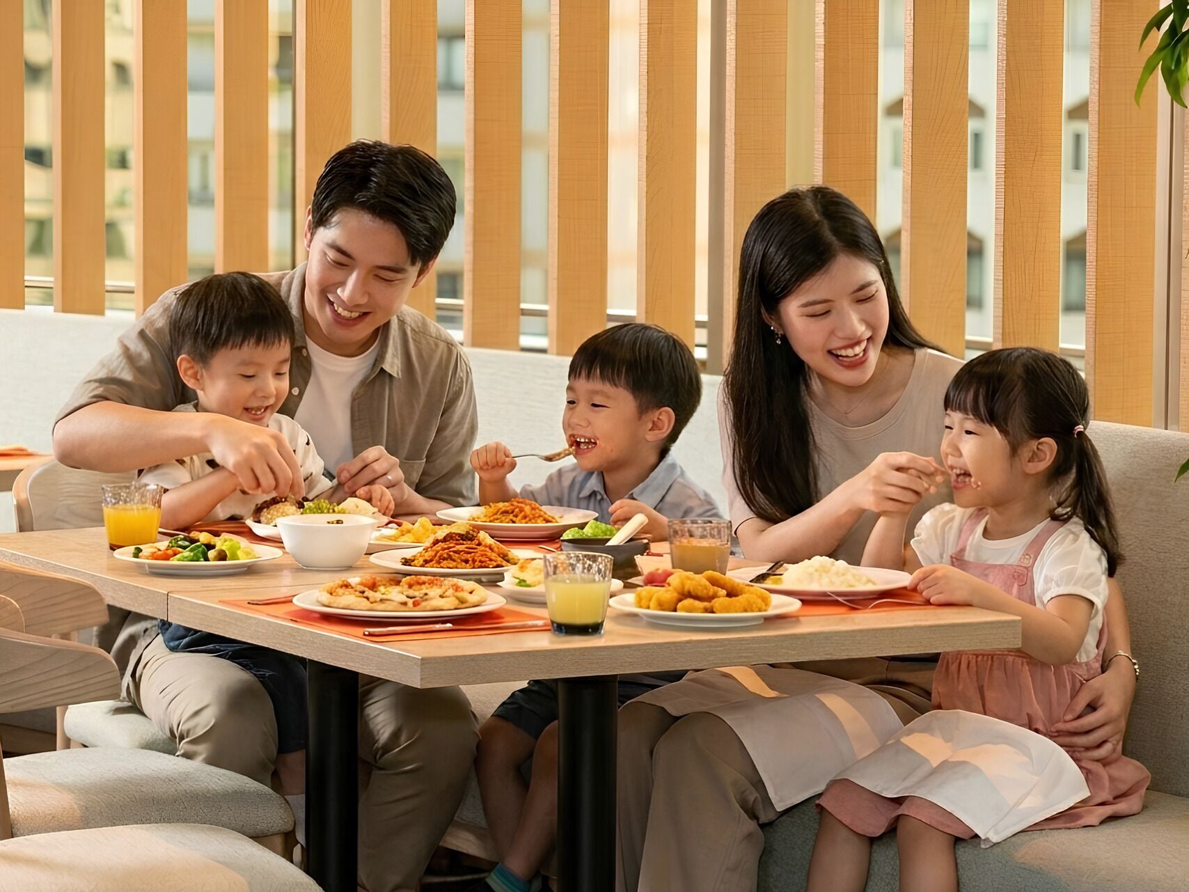 A family dining at a table with various dishes, a plant, and a window with vertical blinds.