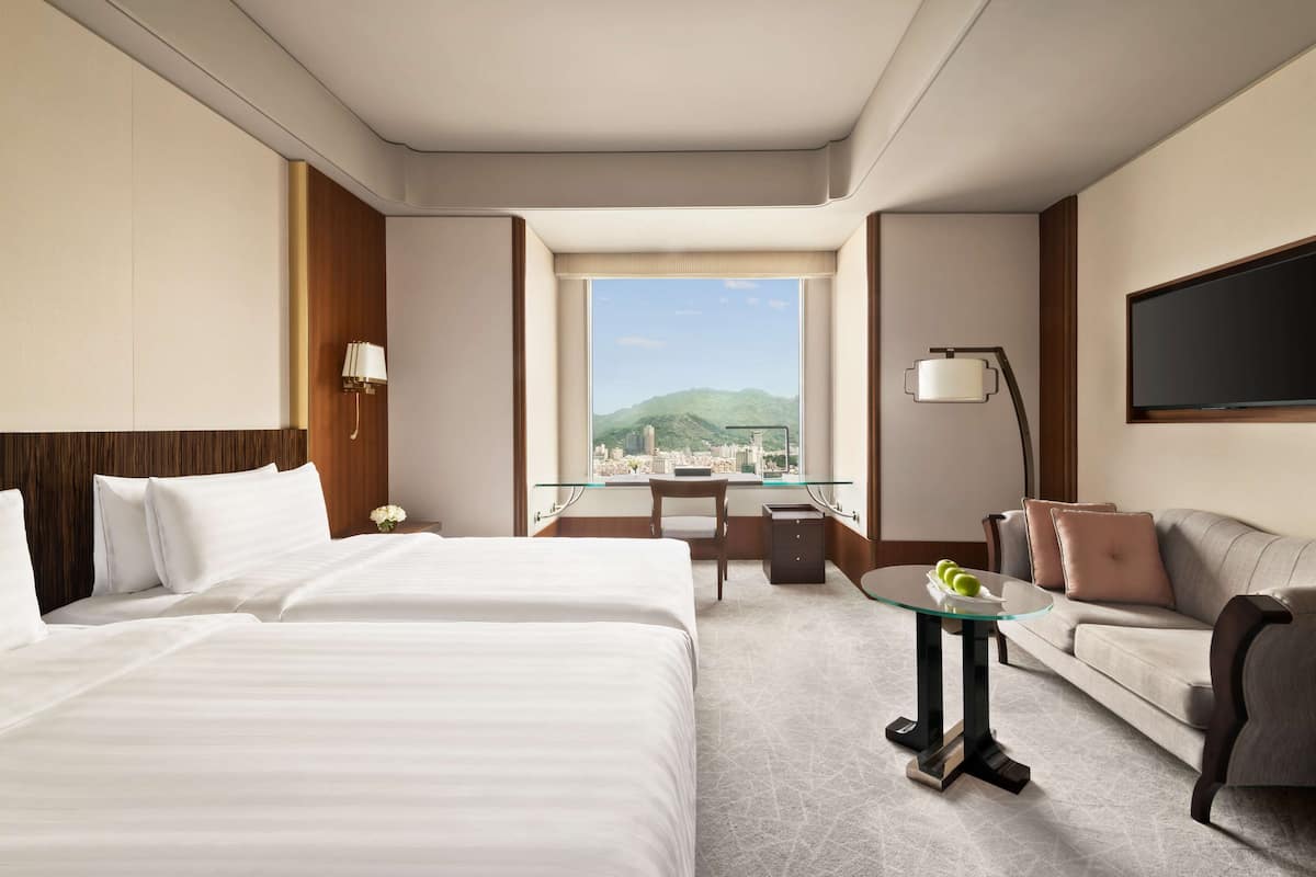 A hotel room with two beds, a sofa, a desk, and a TV.