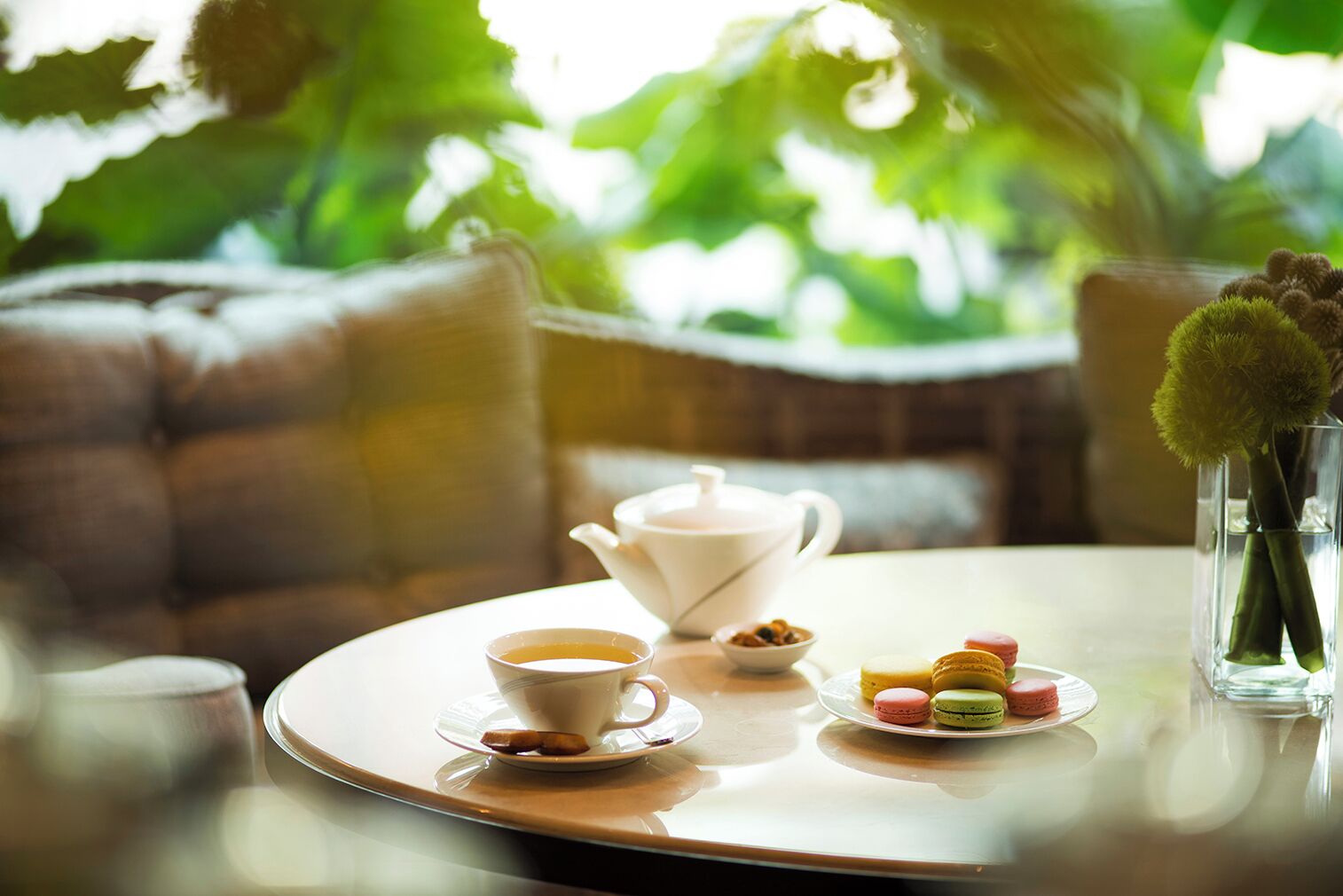 A round table with a teapot, a cup of tea, and a plate of macarons.