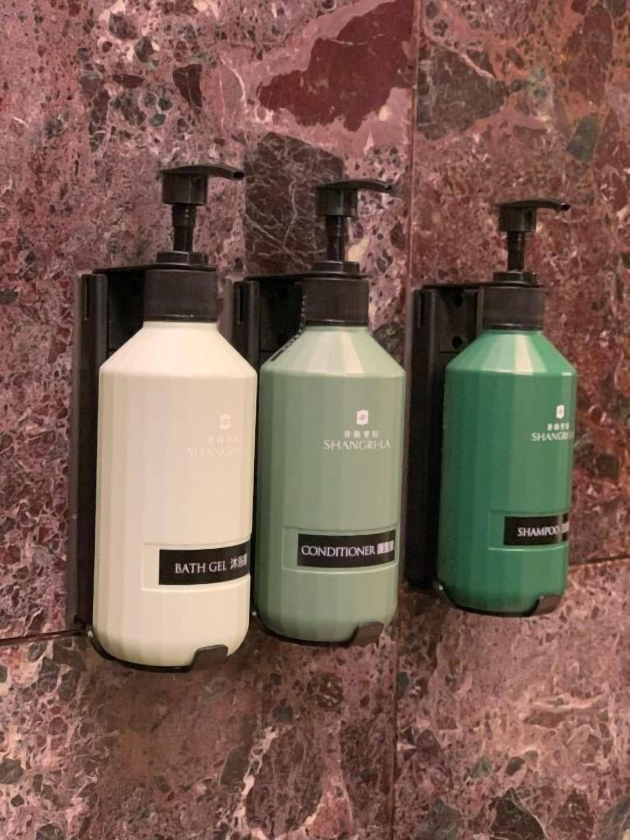 Three bottles of bath gel, conditioner, and shampoo on a marble surface.