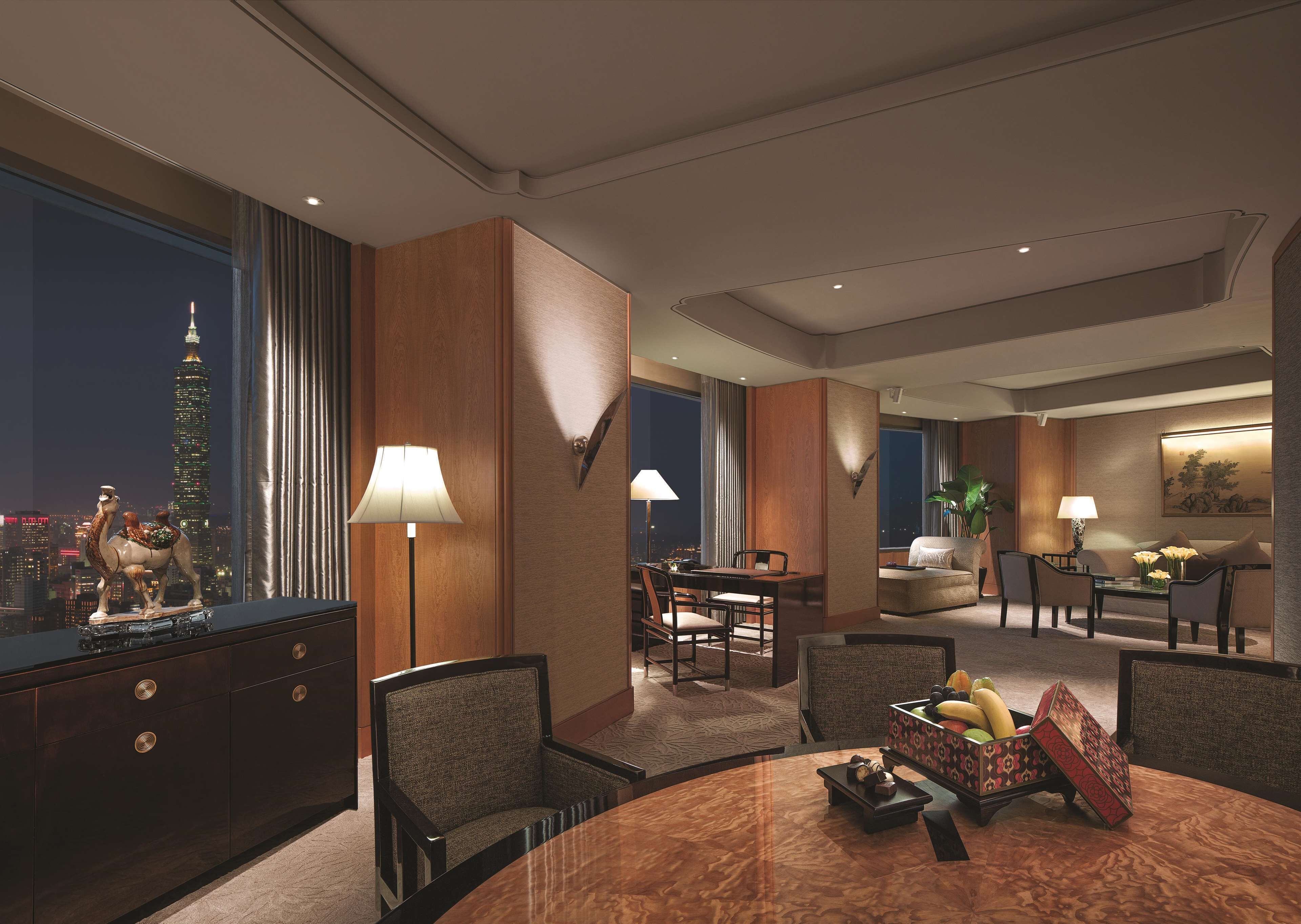 A hotel room with a city view, a dining area, and a living area with a sofa and table.
