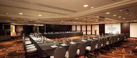 Un salón de conferencias con una larga mesa, sillas y una pantalla para proyector.