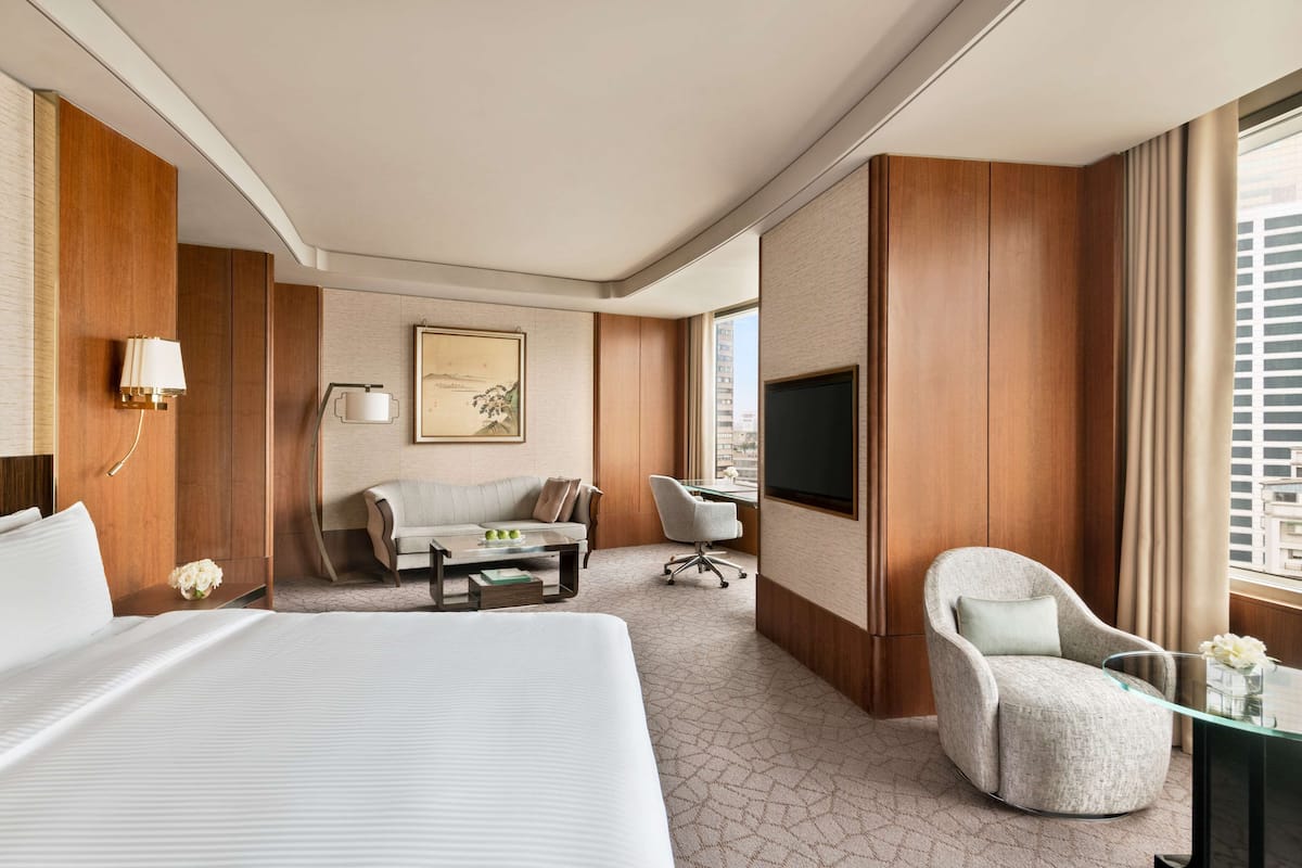 A hotel room with a large bed, a sofa, a desk, and a TV.