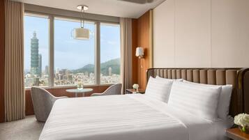 Hotelkamer met een groot bed, een kleine tafel, een stoel en een stadsgezicht door grote ramen.