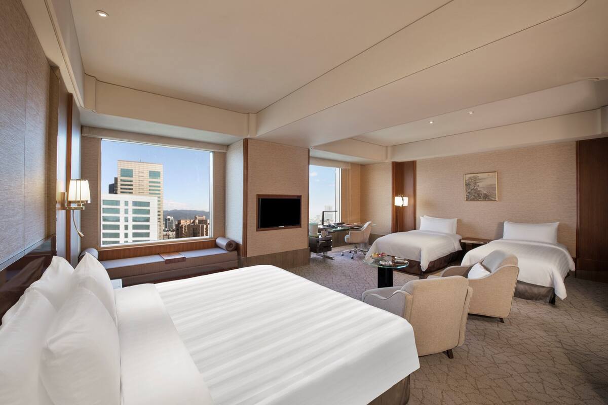 A hotel room with two beds, a desk, a chair, and a TV.