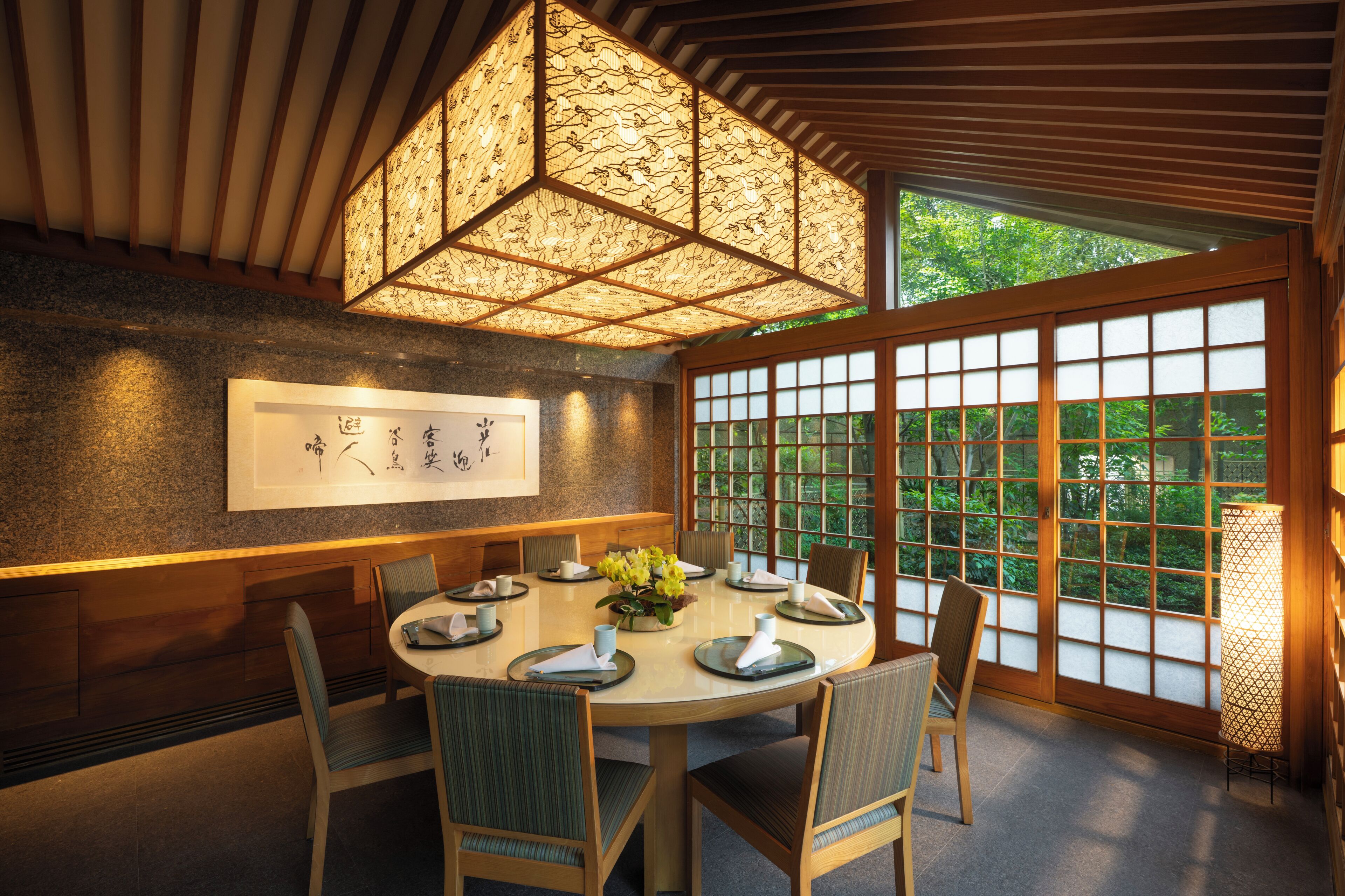 Een traditionele Japanse eetruimte met een ronde tafel, stoelen en een hangende lamp.