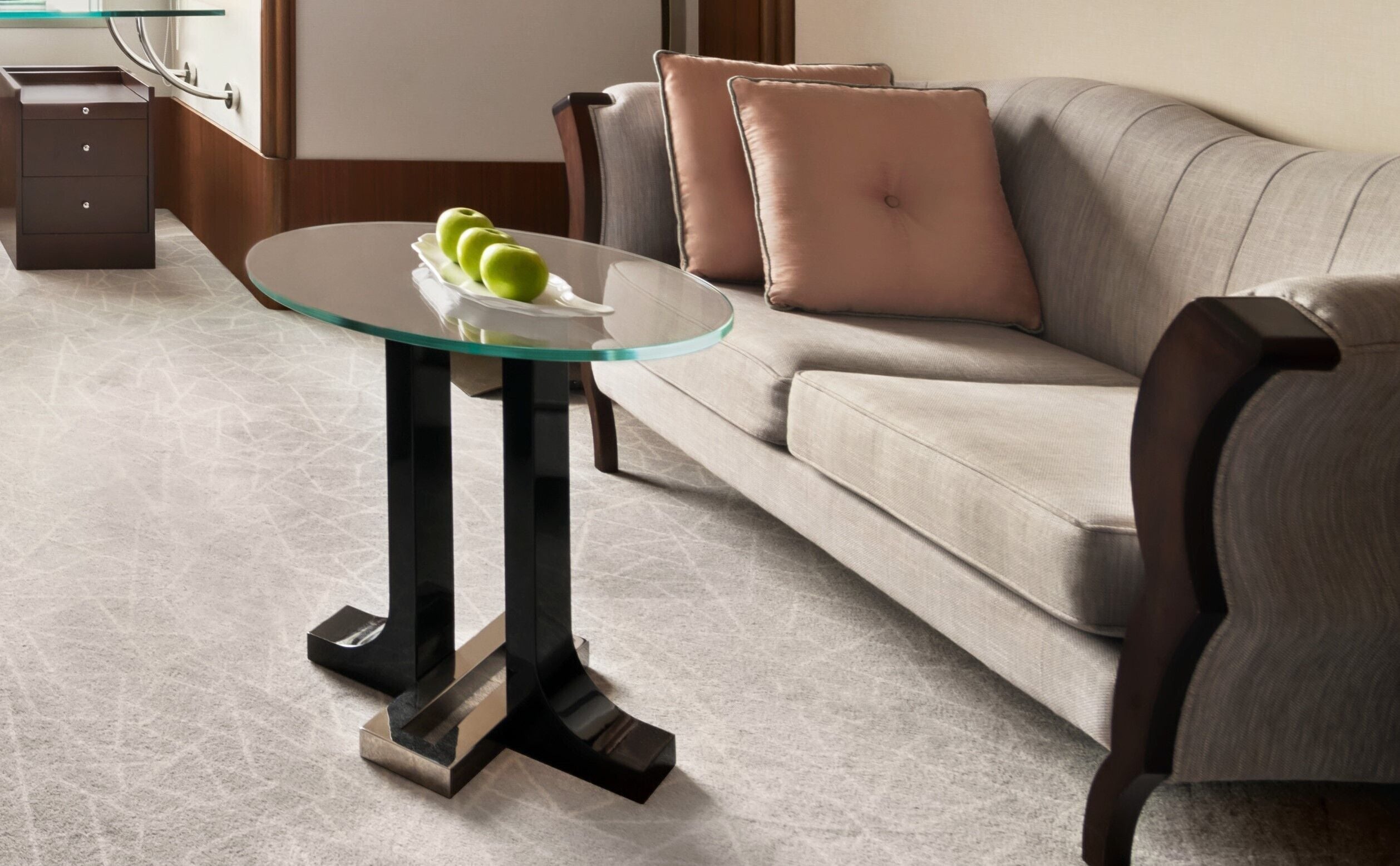 A modern living room with a glass-top coffee table, a grey sofa, and a brown armchair.