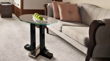 A modern living room with a glass-top coffee table, a grey sofa, and a brown armchair.