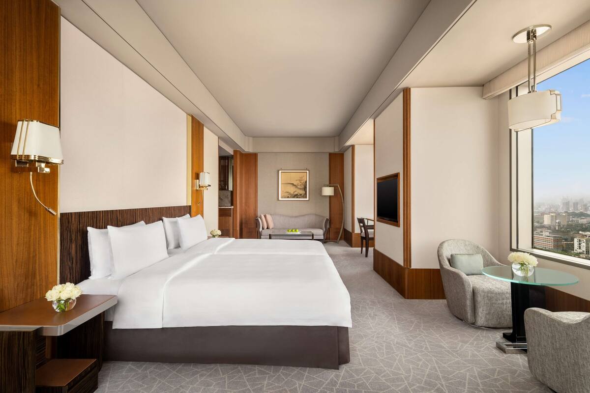 A hotel room with a large bed, a sofa, a glass table, and a city view.