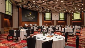 Un salón de conferencias con mesas redondas, sillas negras y un escenario con una pantalla que muestra 'SHANGRI-LA FAR EASTERN TAIPEI'.